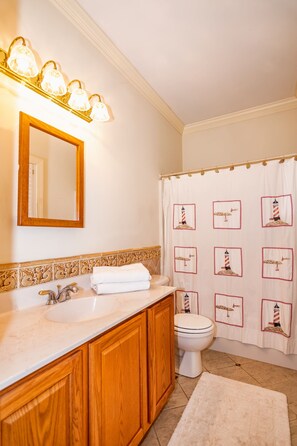 Ein Badezimmer mit Doppelwaschbecken, Holzausbau, einem Spiegel, einer Toilette und einer Duschvorhang mit Leuchttürmotiv.