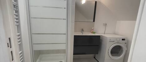 Ett modernt badrum med en dusch utan tröskel, ett handfat, en spegel och en tvättmaskin.