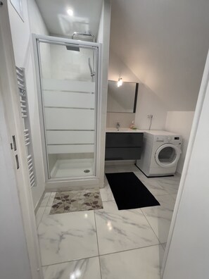 Ein modernes Badezimmer mit begehbarer Dusche, einem Waschbecken, einem Spiegel und einer Waschmaschine.