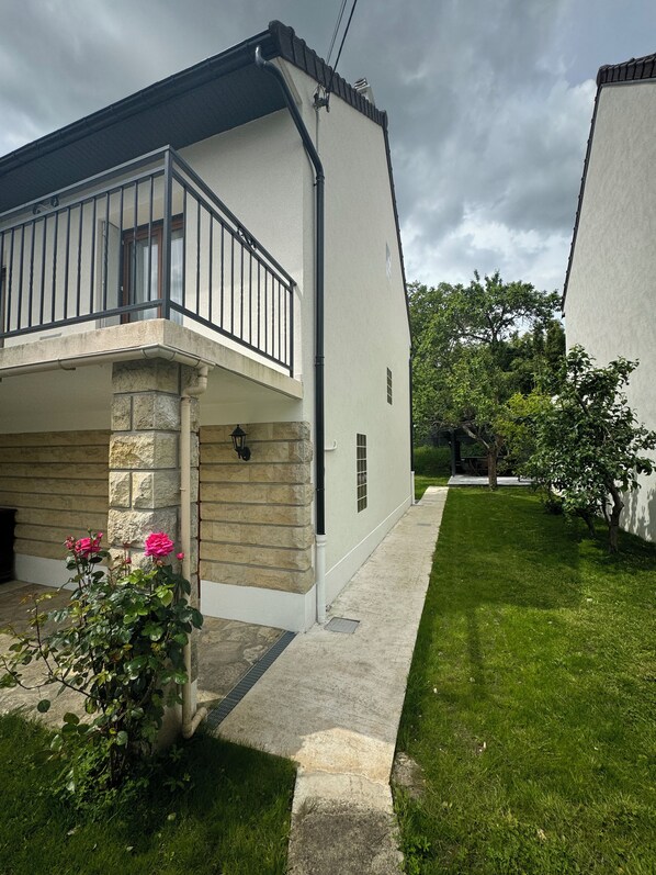 A two-story house with a balcony, stone foundation, and a well-maintained lawn.