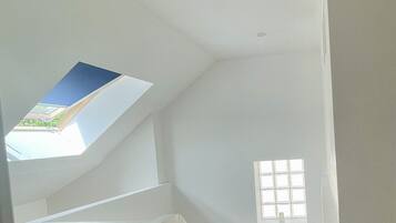 Ein Zimmer mit hohen Decken, einem Oberlicht, einem kleinen Fenster und einer Holztreppe.