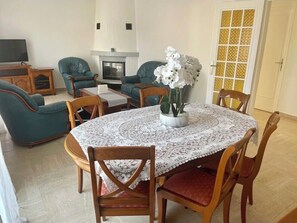 Ein Essbereich mit einem runden Tisch, bedeckt mit einer Spitze-Tischdecke, umgeben von Holzstühlen mit roten Kissen.