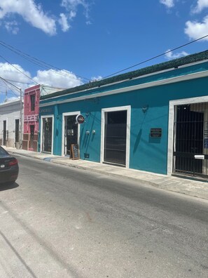 A street view with a teal building, a pink building, and a black car. - Casa La Perlita - Large Luxury Colonial in Centro - Garden, Gazebo, Big Pool ❤️ (Mérida)