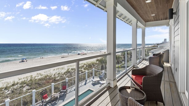 Un balcon avec vue sur la plage et l’océan, des meubles en osier et une piscine.