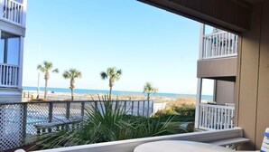 Uma varanda com vista para a praia, palmeiras e um cercado.