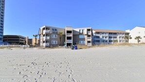 Um hotel à beira-mar com vários andares, varandas e uma praia arenosa em primeiro plano.