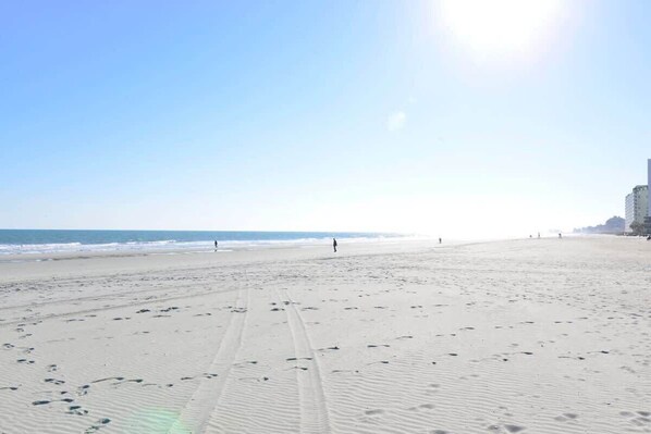 A wide beach with footprints and a person walking.