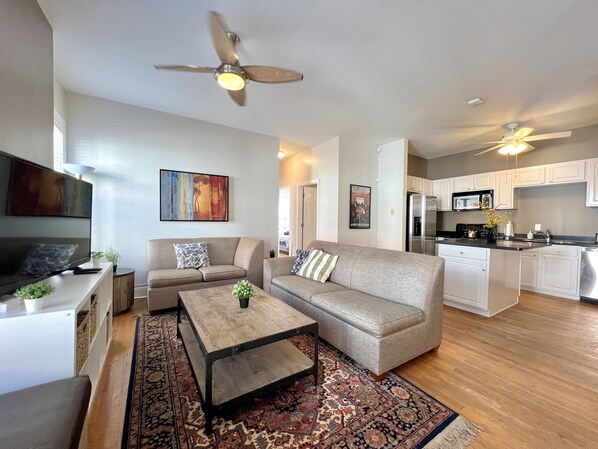 A modern living room with a sofa, coffee table, and a TV. There is a kitchen area with a microwave and stove. - ⌂ Elevated 2bed 1.5 Bath in a Historic 1913 Building ⌂ (Atlanta)