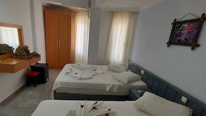A hotel room with two beds, a wooden wardrobe, a mirror, a small table with a red chair, and a picture on the wall. - Pamukkale Hotel (Didim)