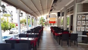A covered outdoor seating area with checkered flooring and tables with red tablecloths. - Pamukkale Hotel (Didim)