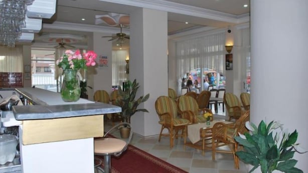 A dining area with wooden chairs and a table, a kitchen area with a counter and a sink, and a large window with blinds. - Pamukkale Hotel (Didim)