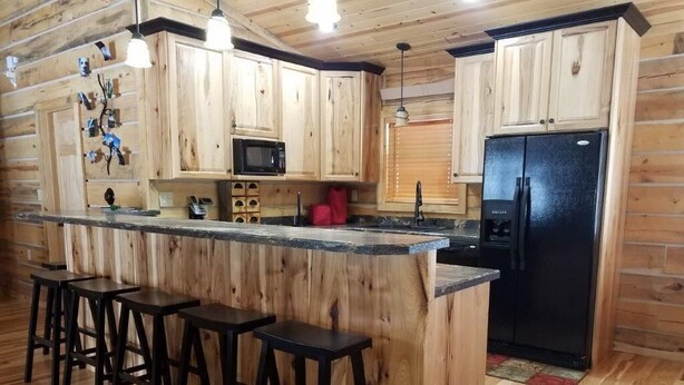 Una cocina con gabinetes de madera, un refrigerador negro, un microondas y una barra con taburetes.