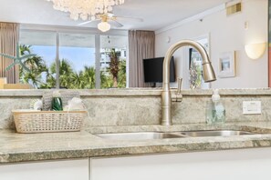 A modern kitchen with a granite countertop, a stainless steel sink, and a ceiling fan. - Beach time! Destin West Condo Pelican 303 (Fort Walton Beach)
