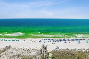 A beach with rows of umbrellas and beach chairs, a sandy shore, and a clear view of the ocean. - Beach time! Destin West Condo Pelican 303 (Fort Walton Beach)