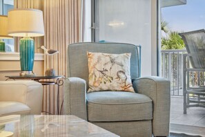 Una sala de estar moderna con un sillón gris, una mesa, una lámpara y un cojín decorativo con motivos naturales.