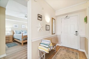 A hotel room with a bed, a bedside table, a chair, a small table with towels, a door, and a wall with framed pictures and a starfish decoration. - Beach time! Destin West Condo Pelican 303 (Fort Walton Beach)