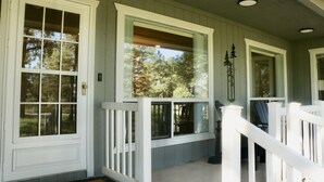 A porch with white railings and large windows overlooking a wooded area.