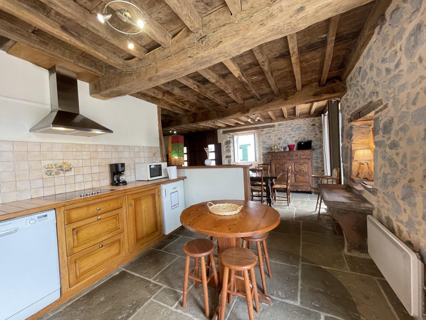 A rustic kitchen with wooden beams, a stone wall, and a tiled backsplash.
