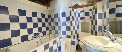 Un baño con baldosas azules y blancas en damero, una bañera, un inodoro y un lavabo.