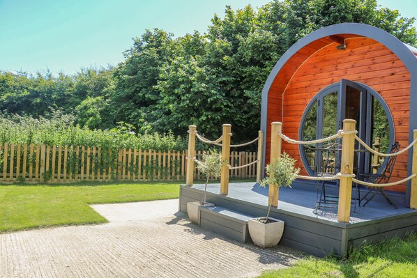 A wooden cabin with a circular window, surrounded by a rope barrier and potted plants.