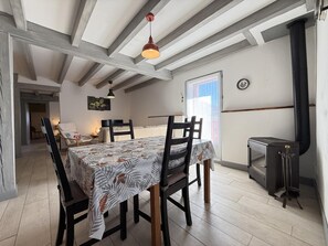 Un coin repas avec une table dressée pour quatre personnes, des chaises en bois, un luminaire suspendu, une cheminée et une vue par la fenêtre.