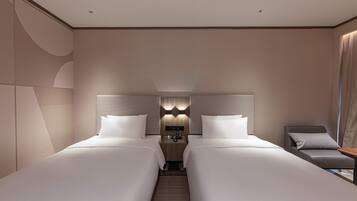 A hotel room with two beds, a nightstand, a chair, and a wall-mounted lamp.