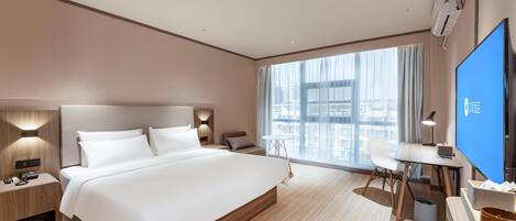 A modern hotel room with a large bed, a desk, a chair, a TV, and a window with a city view.