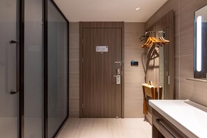 A modern bathroom with a wooden door, a mirror, and a towel rack with hangers. - Hanting Hotel (Changzhou)