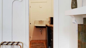 Un corridoio stretto che porta a una cucina con un lavandino, una piccola finestra e una TV su uno scaffale.