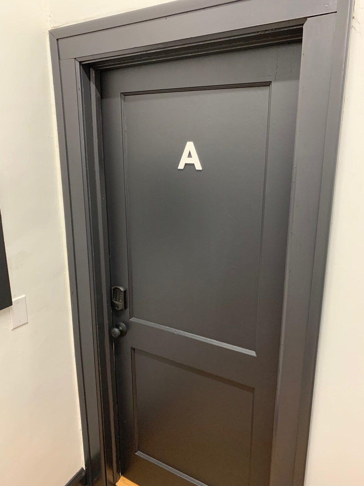 En mörkfärgad dörr med en vit bokstav ”A” på sig, ett dörrhandtag och ett nyckelhål.