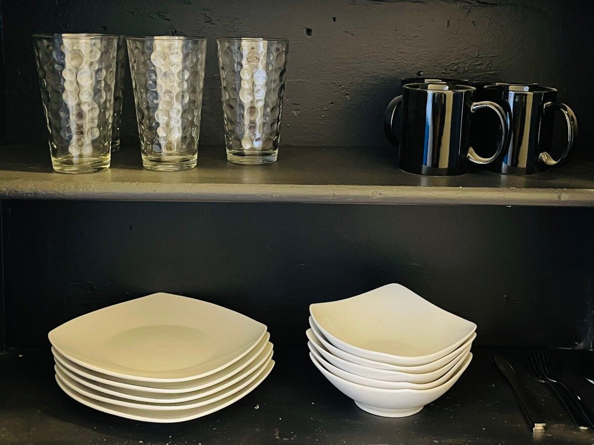 Una repisa de cocina con platos y vasos apilados.