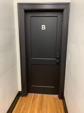 Une porte noire ornée d’un « B », une poignée de porte et un plancher en bois.
