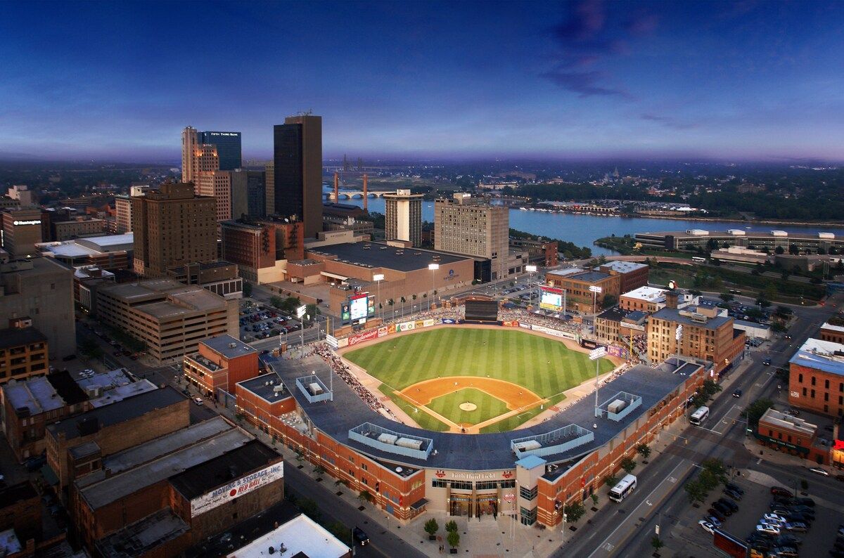A baseball stadium surrounded by urban buildings, with a river in the background.