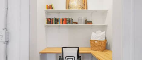 A small office space with a desk, chair, shelves with books, and a picture frame.