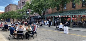 An outdoor dining area with tables and chairs, surrounded by brick buildings and trees.