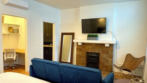 A hotel room with a large bed, a blue sofa, a TV mounted above a fireplace, and a chair by the window. - EZ Check-in and Check-Out, Perfect for a Night Downtown! (Toledo)