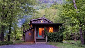 A rustic cabin with a front porch, surrounded by dense forest. - Creekside Cabin with Hot Tub & Wood-Burning Stove (Lanesville)