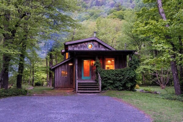 A rustic cabin with a front porch, surrounded by dense forest. - Creekside Cabin with Hot Tub & Wood-Burning Stove (Lanesville)
