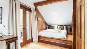 A bedroom with a sloped ceiling, a wooden bed, a desk with a lamp, and a view through a glass door. - Creekside Cabin with Hot Tub & Wood-Burning Stove (Lanesville)