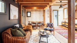 A cozy living area with a leather sofa, a small table, and a patterned rug. - Creekside Cabin with Hot Tub & Wood-Burning Stove (Lanesville)