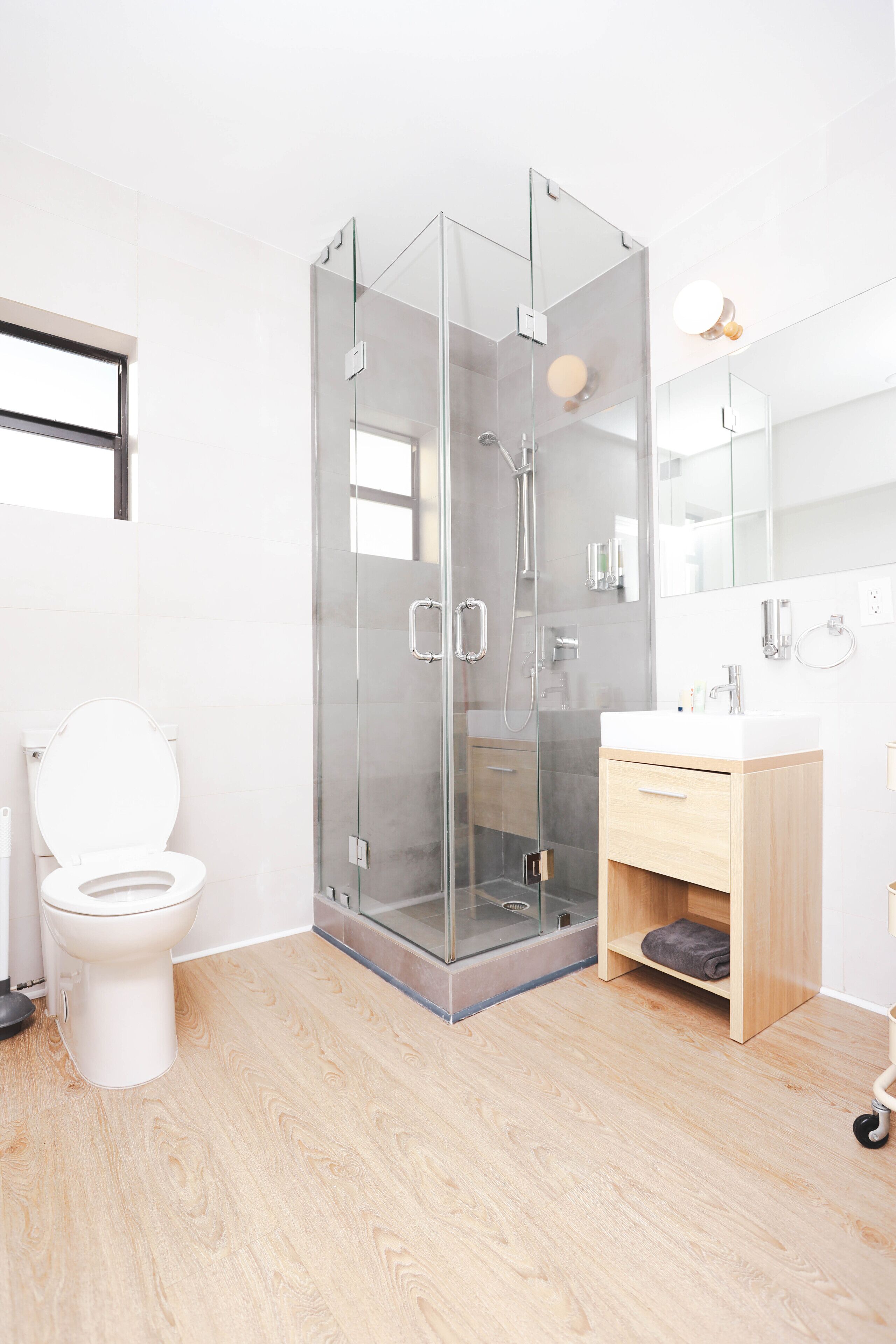 A modern bathroom with a glass-enclosed shower, a white toilet, and a wooden vanity.