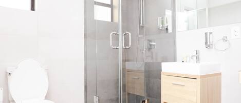 A modern bathroom with a glass-enclosed shower, a white toilet, and a wooden vanity.