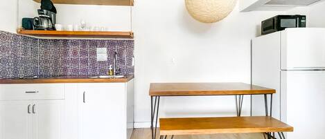 A modern kitchen with white cabinets, patterned backsplash, wooden shelves, a hanging light, and a minimalist table.