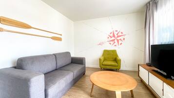 Un salon moderne avec un canapé gris, un fauteuil vert, une table basse en bois et un téléviseur posé sur un meuble en bois.