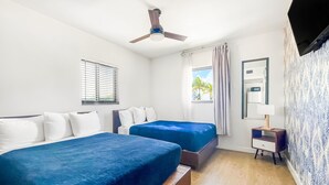 Une chambre d’hôtel avec deux lits, un ventilateur de plafond, une fenêtre avec des rideaux, une table de chevet et un miroir.