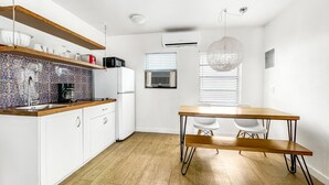 Une cuisine moderne avec des armoires blanches, un comptoir en bois et un pare-feu décoré. On y trouve une table à manger avec des chaises et un luminaire suspendu.