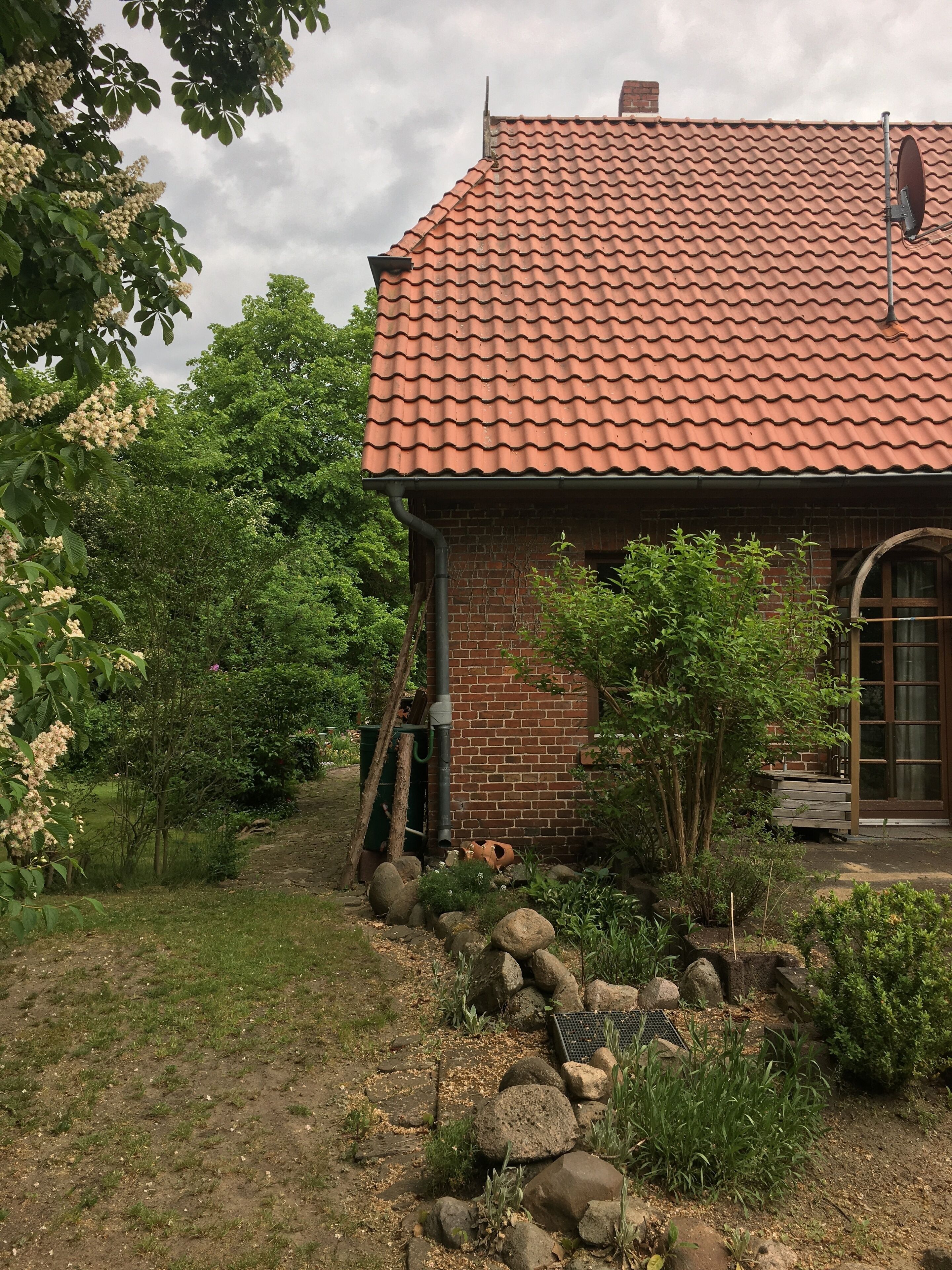 Une maison en briques avec un toit en tuiles, entourée d’un jardin agrémenté de rochers et de plantes.