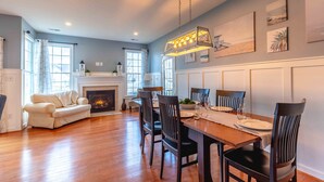 Un salón amplio con chimenea, un comedor con mesa y sillas de madera, y un ventanal que proporciona luz natural.