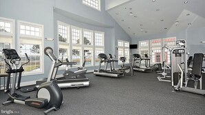 Un gimnasio espacioso con numerosas cintas de correr, elípticas y estaciones de pesas. Amplias ventanas ofrecen luz natural y vistas al exterior.