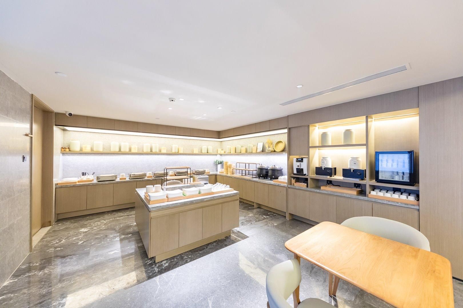 Una habitación de hotel moderna con suelo de mármol, muebles de madera, una isla central con alimentos y un televisor a la derecha.